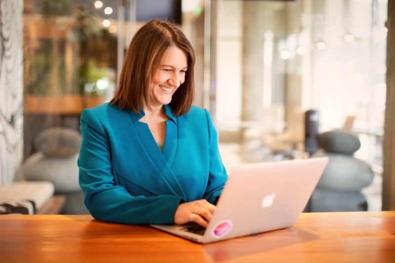 An Image of A woman A leadership coach smiling while working on laptop