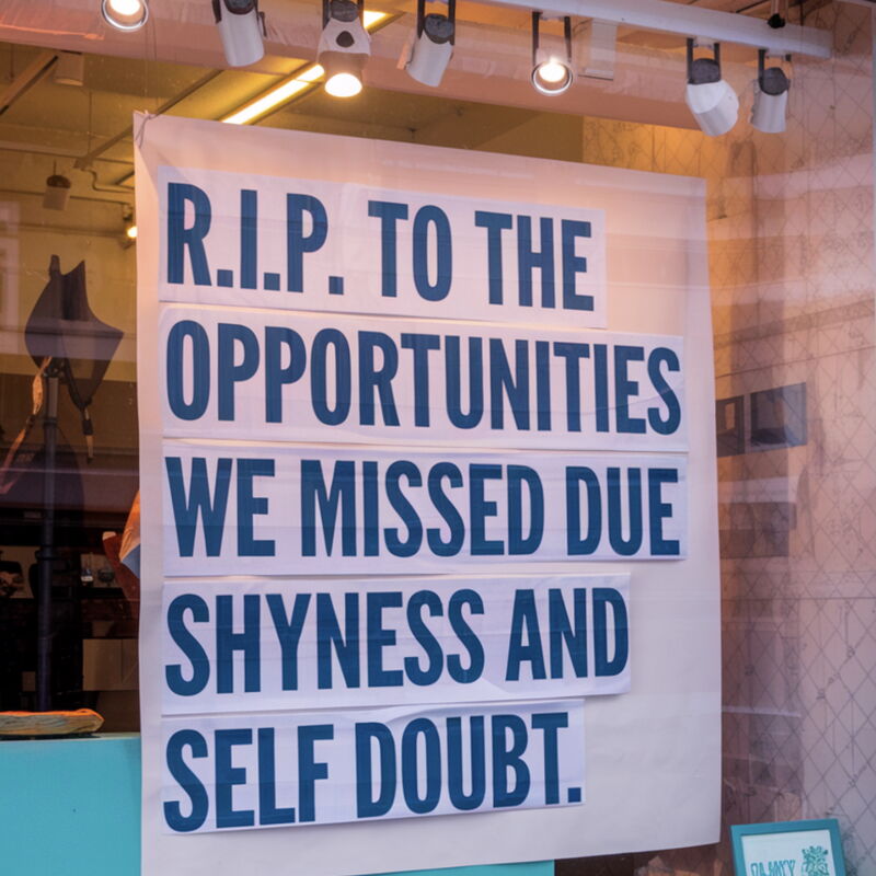 A large sign in a window reads "R.I.P. TO THE OPPORTUNITIES WE MISSED DUE SHYNESS AND SELF DOUBT."