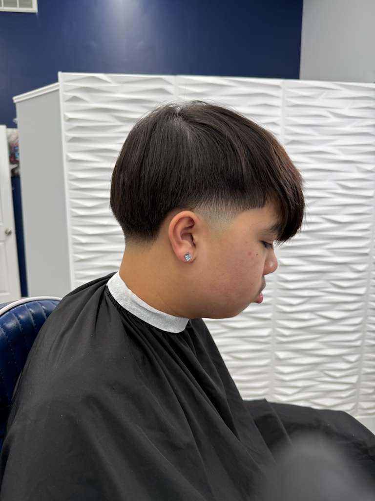 Barber and apprentice reviewing clipper techniques, mid-action training shot, documentary style showing craft transmission.