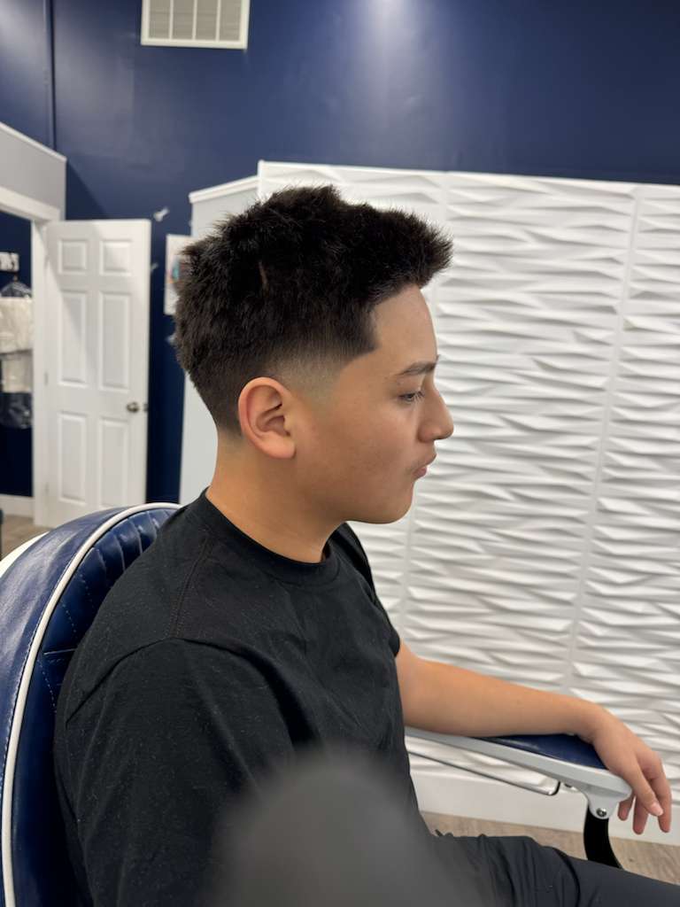 Shot of a stylist shaping a beard with a straight razor, steam and lather visible, focused close-up on hands and razor edge, dramatic lighting.