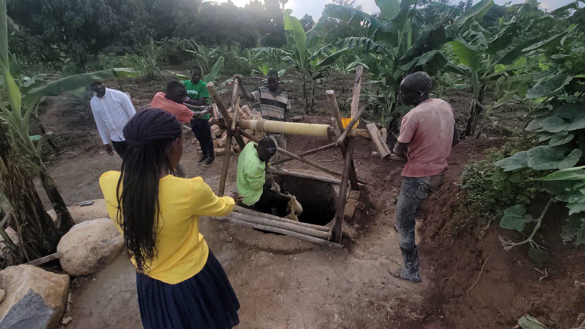Three smiling children standing in front of a brick building under construction in rural Uganda at sunset
