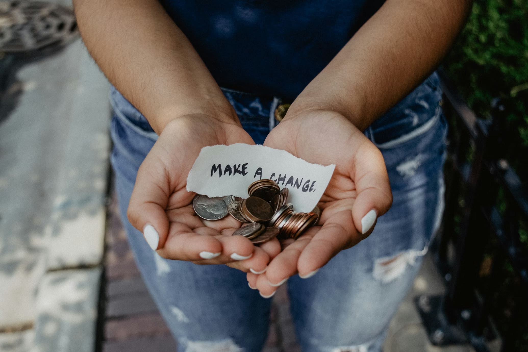 Close-up of hands holding a pile of coins and a handwritten note that reads 'MAKE A CHANGE'