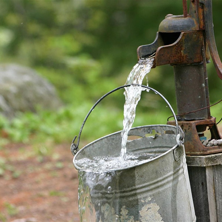 Fresh water flowing from an old hand pump into a metal bucket outdoors