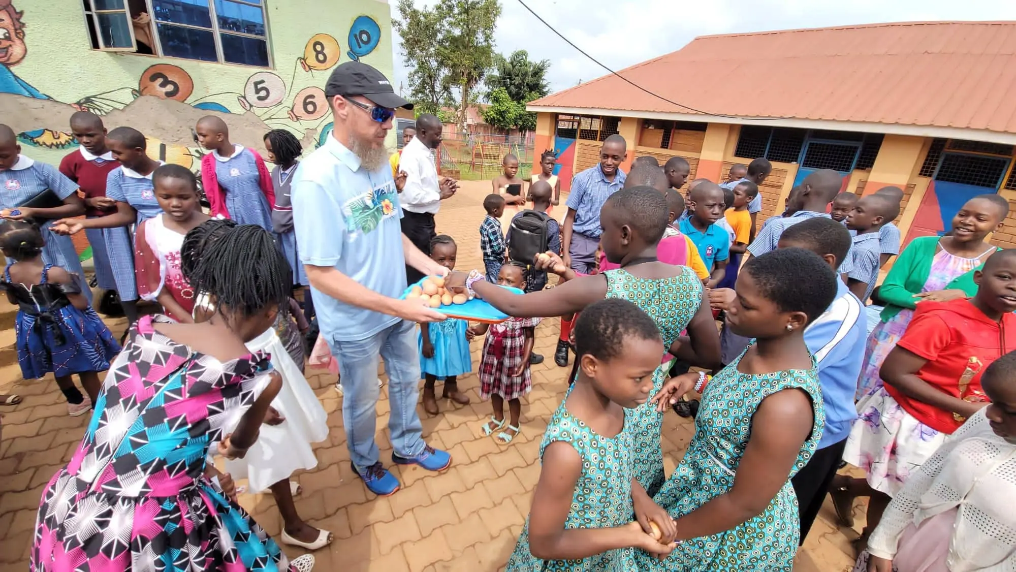 Children gathered outside a school receiving food from an adult during a community activity.