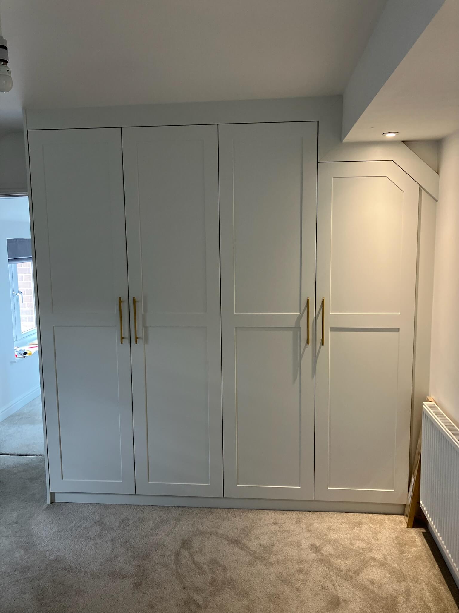 Bespoke white shaker-style fitted wardrobe in a loft bedroom, custom-built by JAX Bespoke to maximize sloping ceiling space with elegant panel detailing and polished chrome handles Bespoke white shaker-style fitted wardrobe in a loft bedroom, custom-built by JAX Bespoke to maximize sloping ceiling space with elegant panel detailing and polished chrome handles