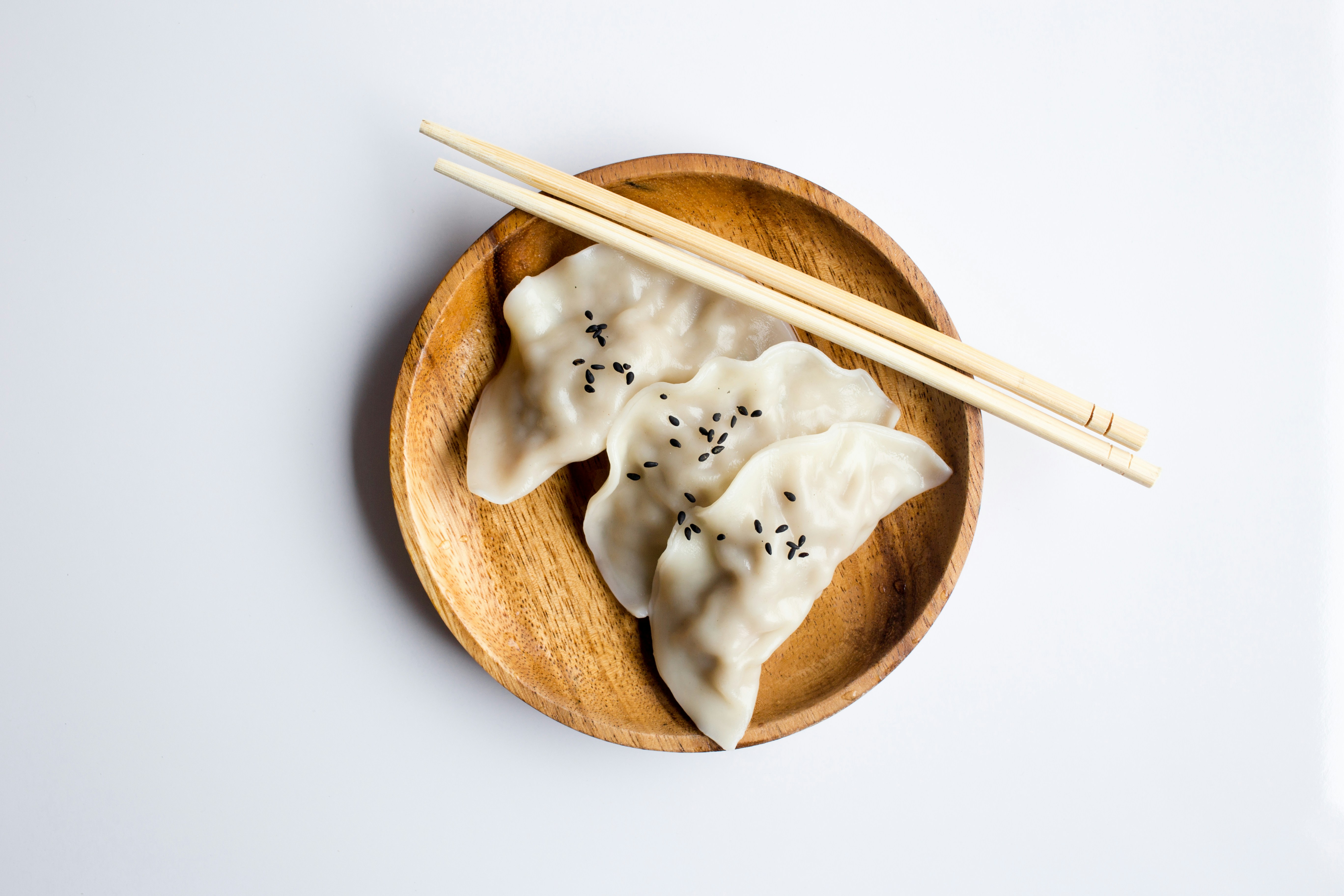 A small wooden bowl is filled with three small dumplings.  A pair of wooden chopsticks rest on the bowl.