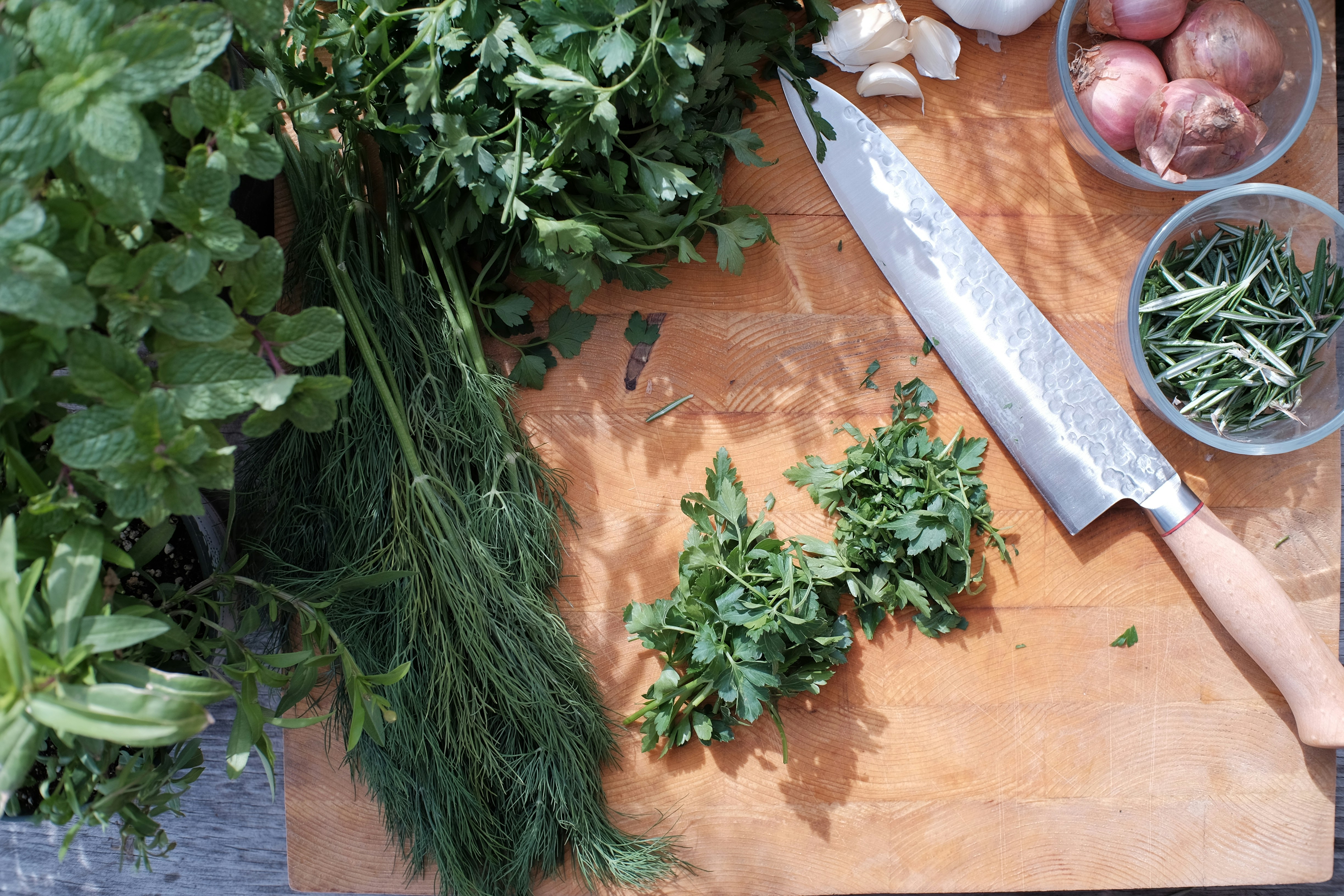 A large knife rests on a wooden chopping block, surrounded by various green herbs.