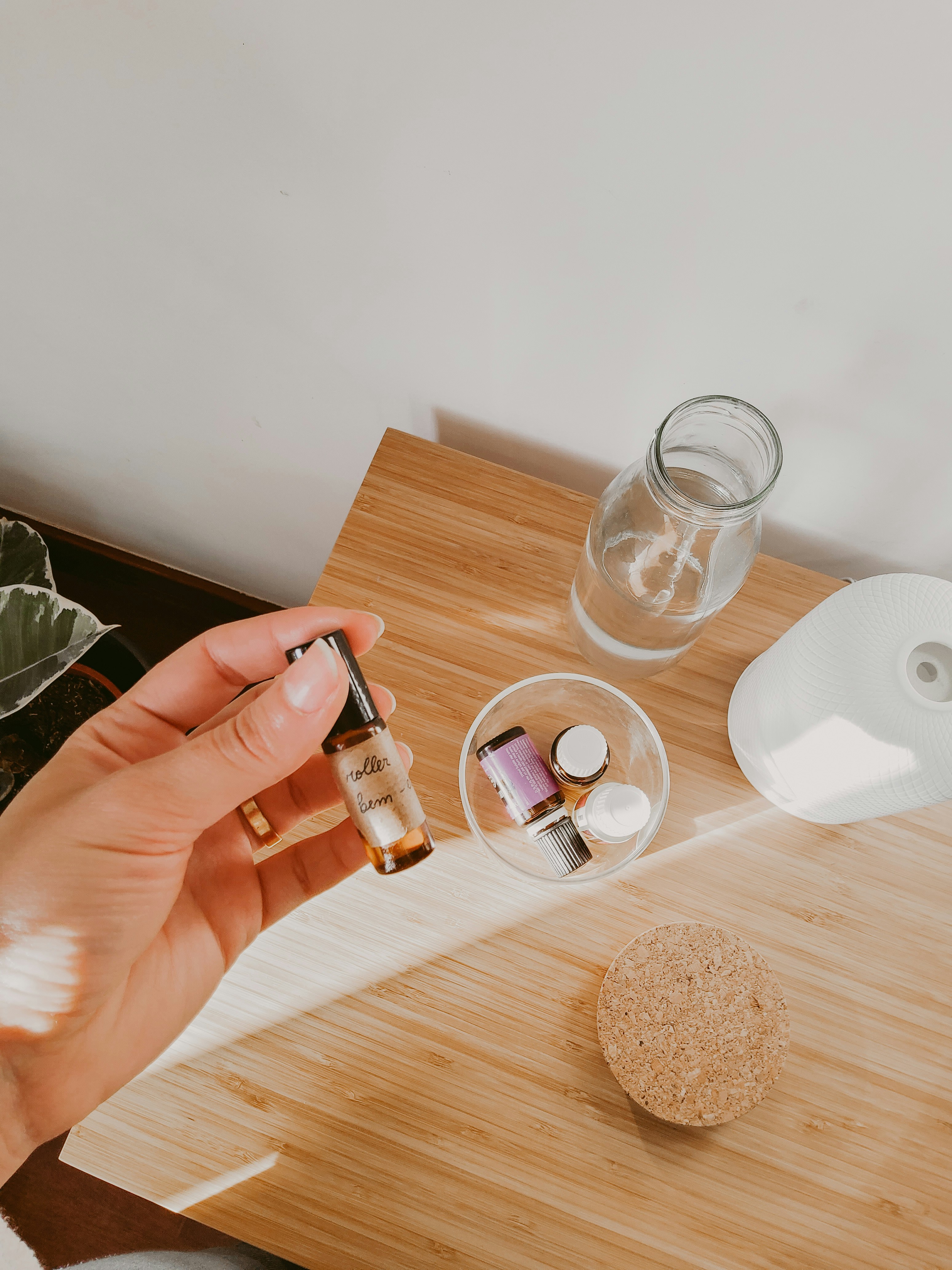 Small bottles of essential oils are on a wooden table, alongside a glass of water.