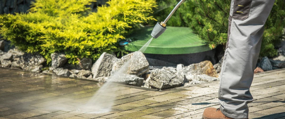Worker using a pressure washer to clean outdoor patio paving stones