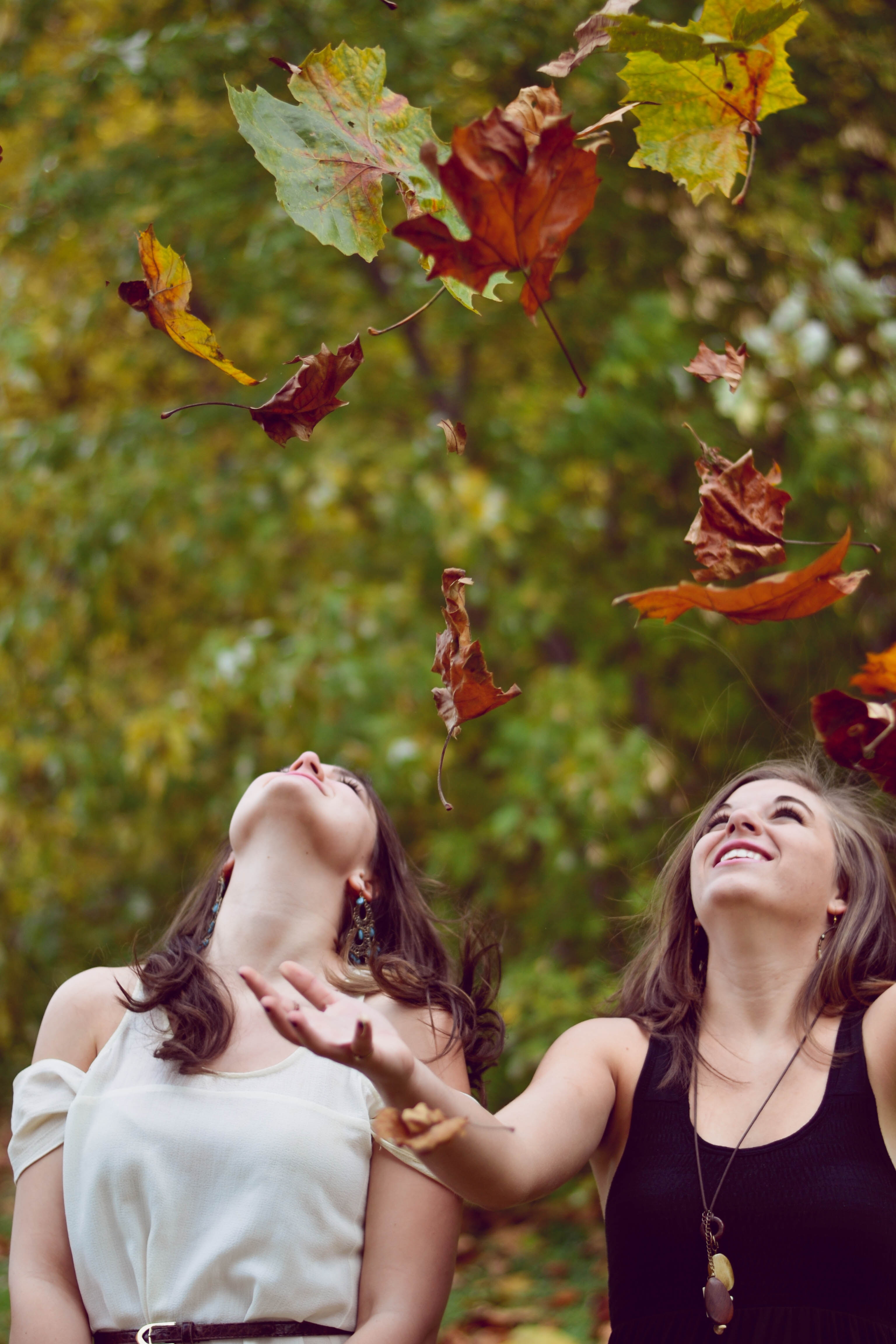 Women smiling outdoors as autumn leaves fall around them Women smiling outdoors as autumn leaves fall around them