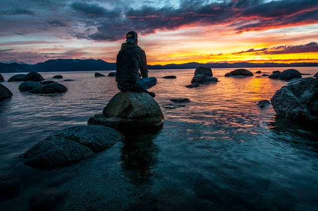 image of a man sitting on rocks near the water