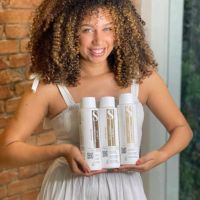 Model with curly hair holding S Professional My Crown line — professional products designed to define curls, reduce frizz, and enhance natural texture