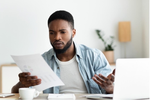 Man reading documents at home, analyzing income sources, spending habits, assets, liabilities, and wealth to understand financial situation.