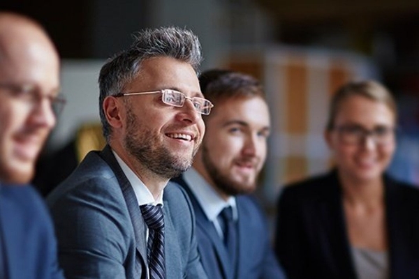 A cheerful group of business professionals wearing suits and smiling, representing success and camaraderie in the workplace.