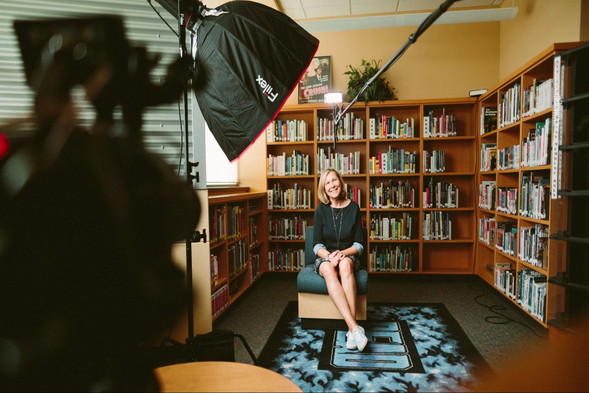 Woman sitting in a library being recorded with professional lighting equipment.