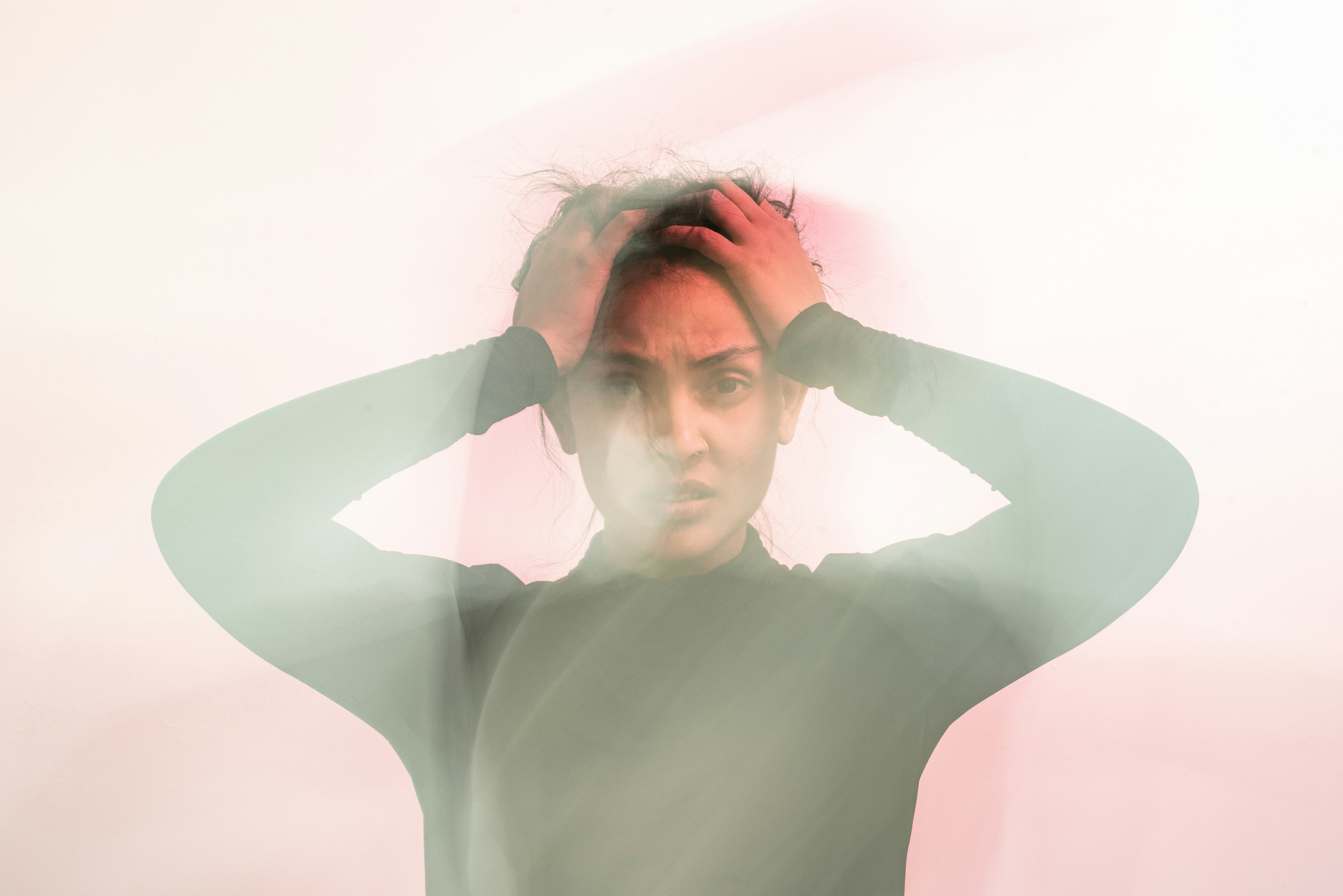 A person with hands on their head, looking overwhelmed or stressed, with a blurred, ghostly effect creating a sense of confusion or inner turmoil.