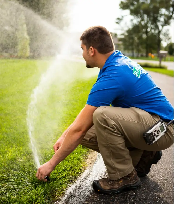 Technician inspecting irrigation sprinkler during maintenance in Rochester NY