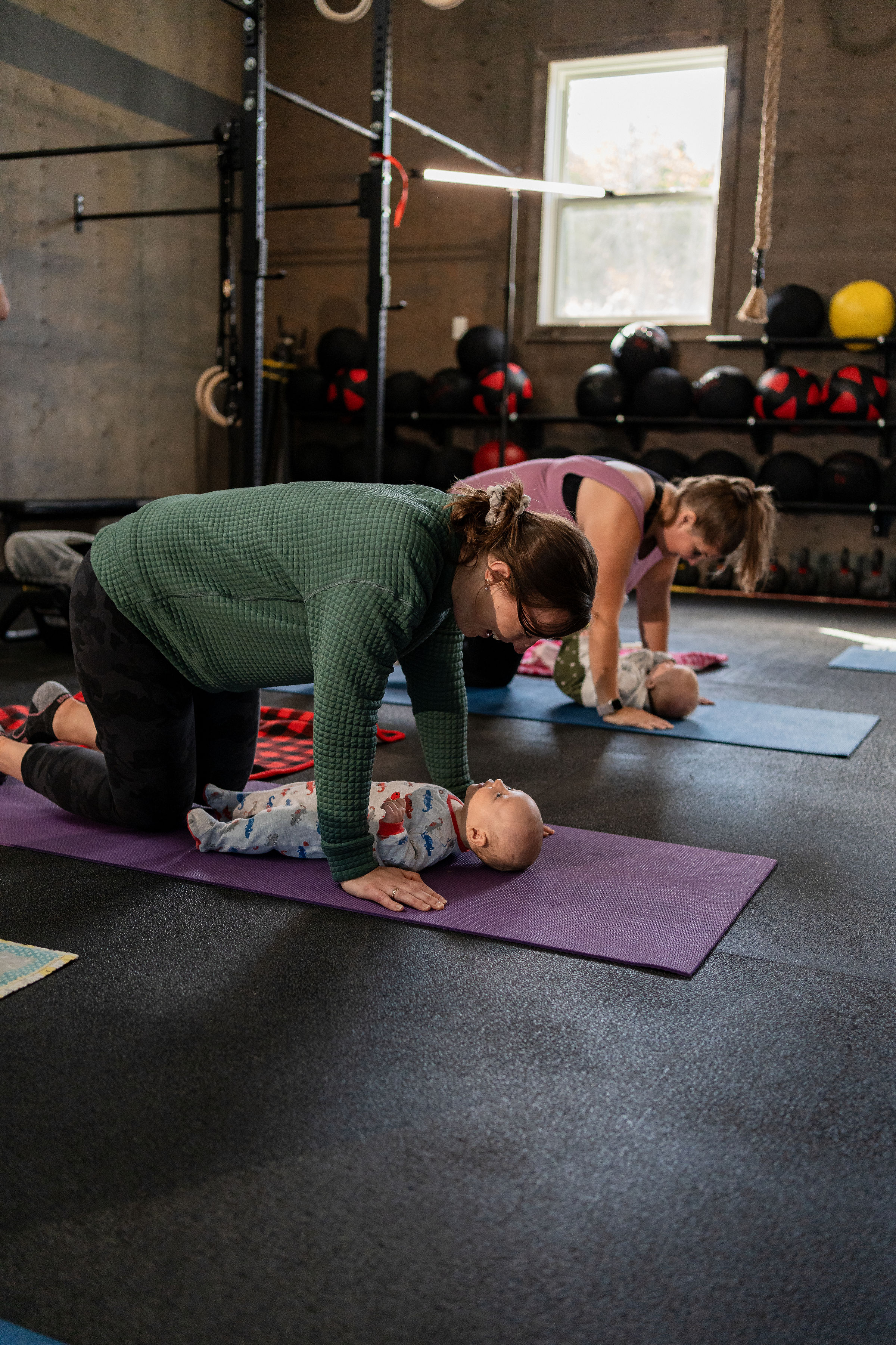 Image of two postpartum women with their babies in a yoga position. They are in a Stittsville gym that is open and inviting and are enjoying effective exercise with their babies.