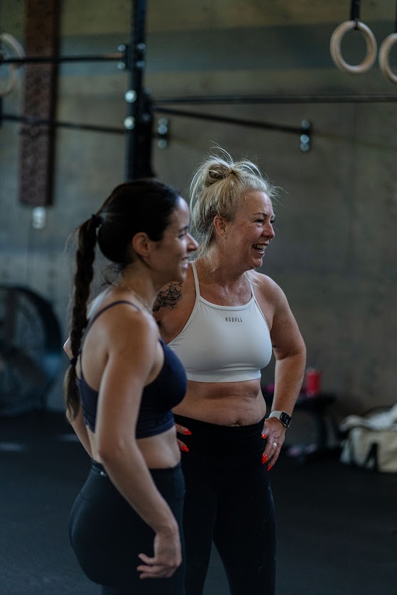 Image of two women smiling after a workout. They are in a Stittsville gym that is open and inviting, and look to be very happy for the accountability that comes with working out with a friend.