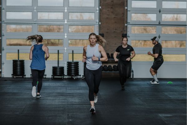 A woman runs with other gym members during a gym class at Between the Bumpers in Stittsville. The gym is clean and has a big, bright window, letting light in from outside.