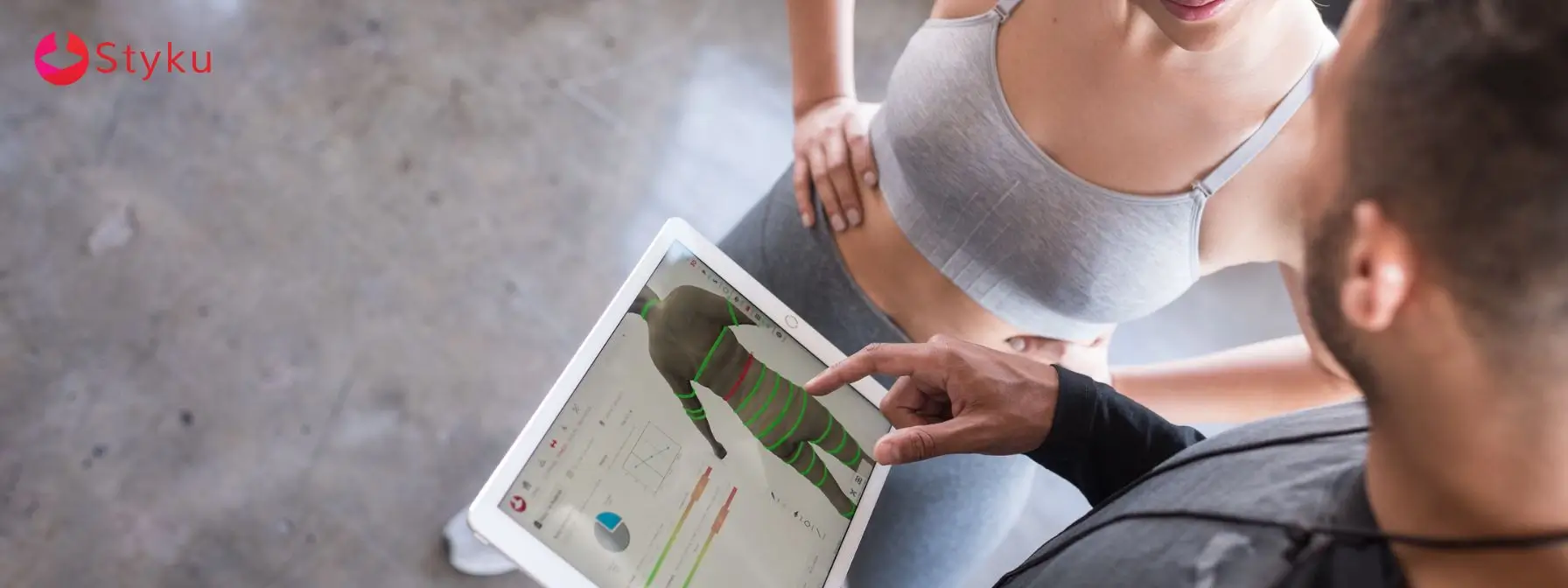 Trainer and client reviewing body composition and visceral fat analysis on Styku 3D body scanner tablet