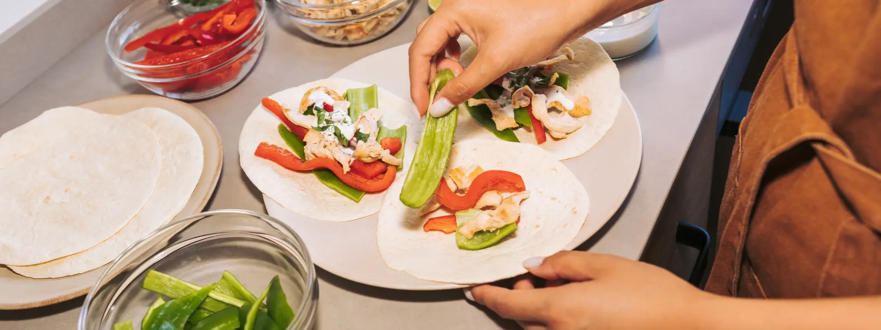 Person preparing healthy chicken wraps with bell peppers, cucumbers, and a yogurt-based sauce on soft tortillas — a quick and balanced meal idea perfect for meal planning and busy lifestyles.