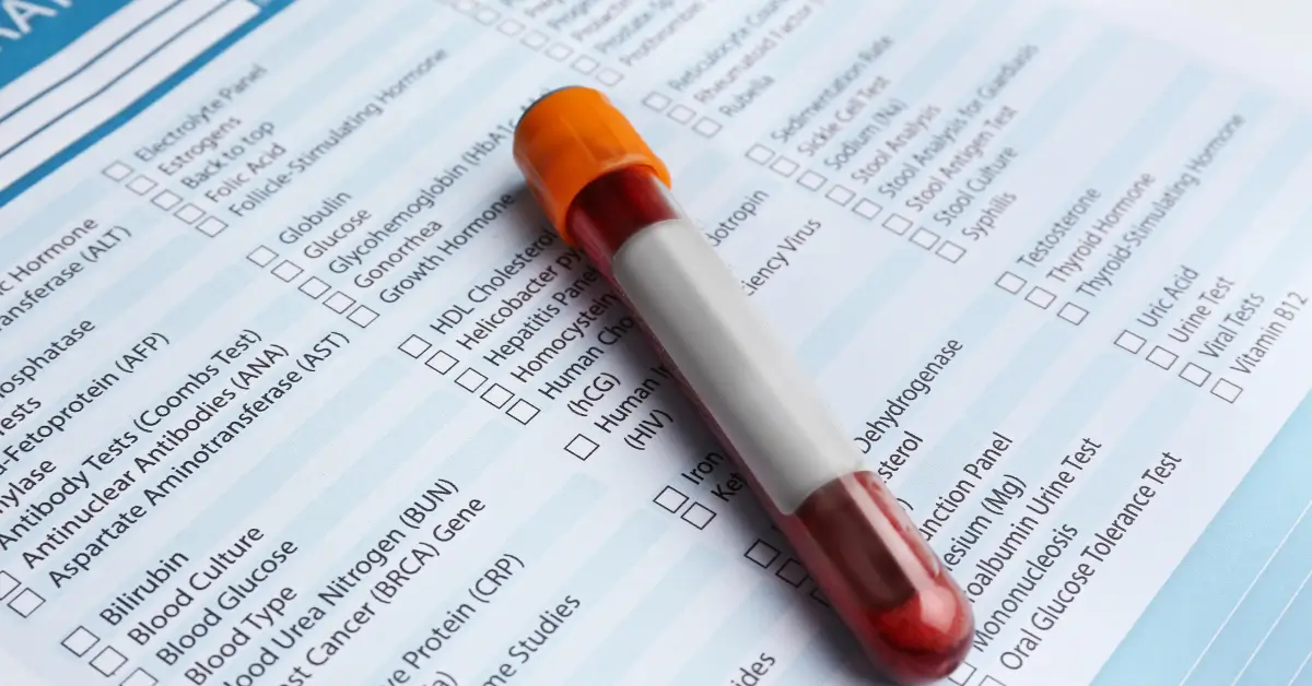 A blood sample tube with an orange cap placed on top of a medical test form listing various laboratory tests and checkboxes.
