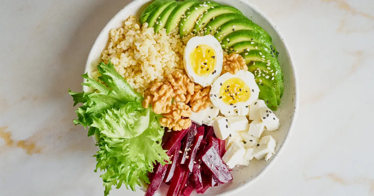 Nutritious bowl with avocado, boiled eggs, walnuts, leafy greens, beets, cheese, and grains, representing an energy-boosting diet to combat post-menopause fatigue. Nutritious bowl with avocado, boiled eggs, walnuts, leafy greens, beets, cheese, and grains, representing an energy-boosting diet to combat post-menopause fatigue.