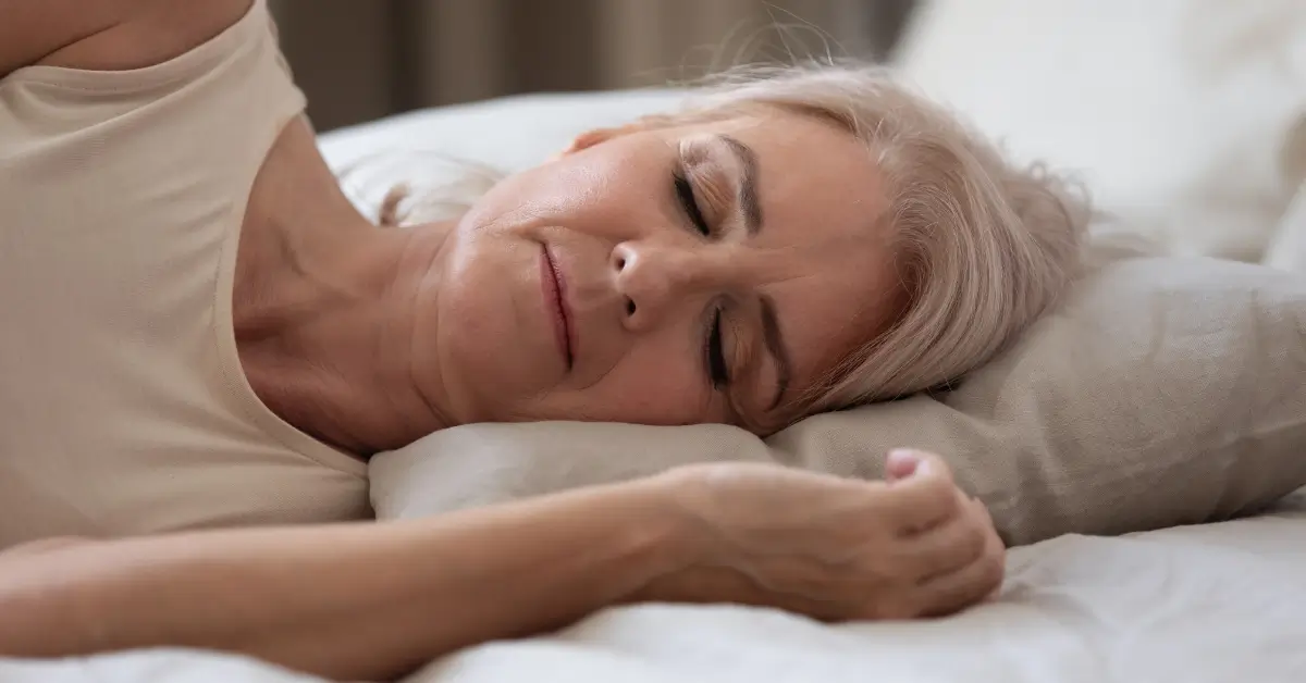 Older woman resting peacefully in bed, highlighting the importance of quality sleep as part of boosting energy and overcoming fatigue after menopause. Older woman resting peacefully in bed, highlighting the importance of quality sleep as part of boosting energy and overcoming fatigue after menopause.