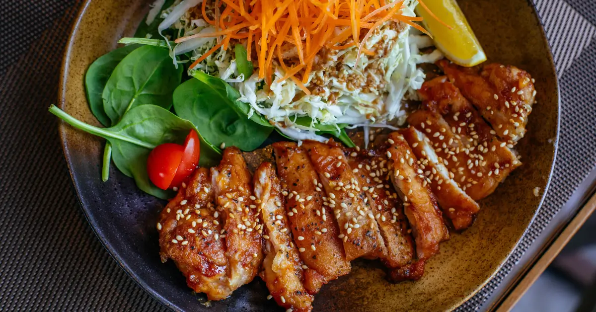 Plate of grilled chicken with sesame seeds, fresh spinach, shredded cabbage, carrots, and tomato, representing a nutrient-rich diet that supports hormone balance and preventive health for adults over 40 in Hurricane, WV.