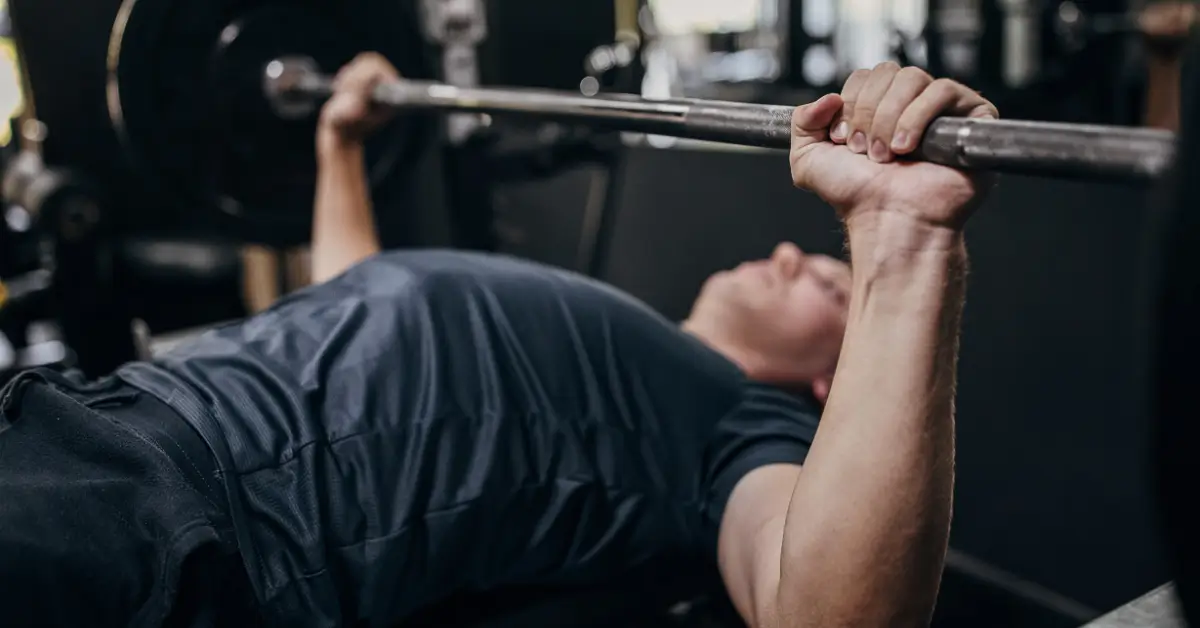 Man performing a bench press exercise in a gym, lifting a barbell while lying on a weight bench.