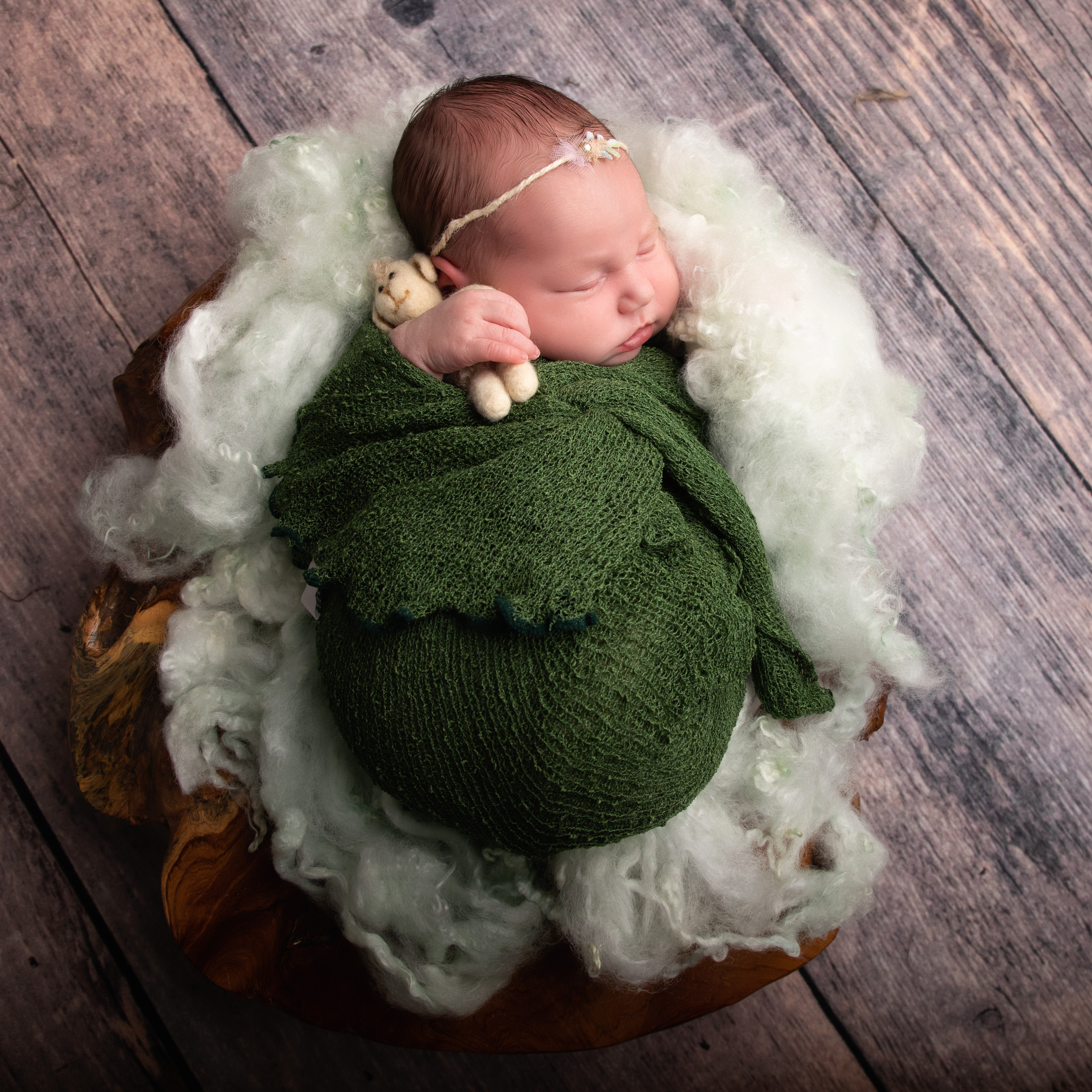 Newborn Rowan wrapped in dark green clutching a felted lamb