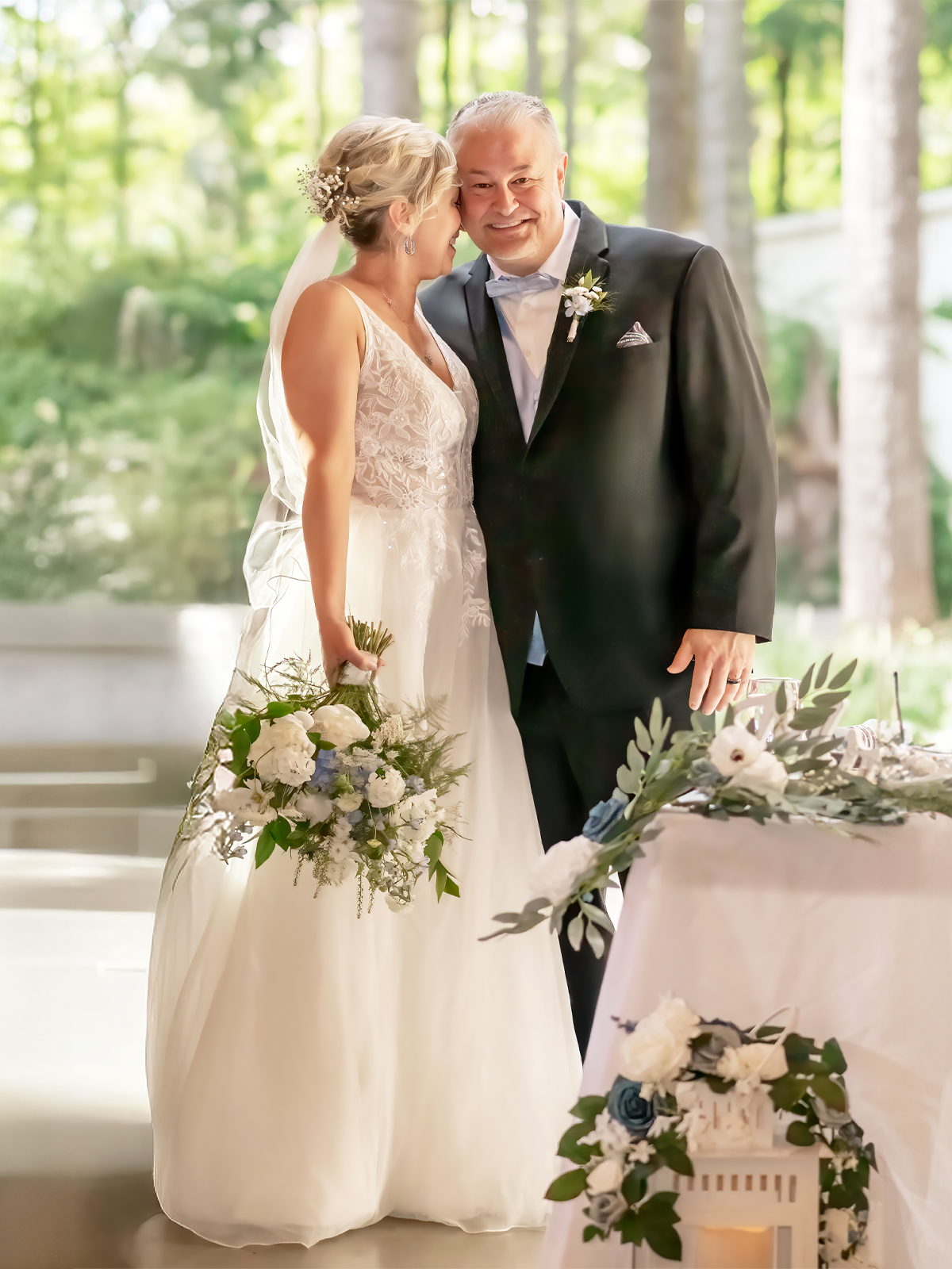 An exquisite bride and groom exchange a tender glance, she in a delicate lace gown with a floral bouquet, he in a sleek black suit, standing before a floral-adorned table, reflecting the meticulous craftsmanship of a wedding photographer in Seattle.