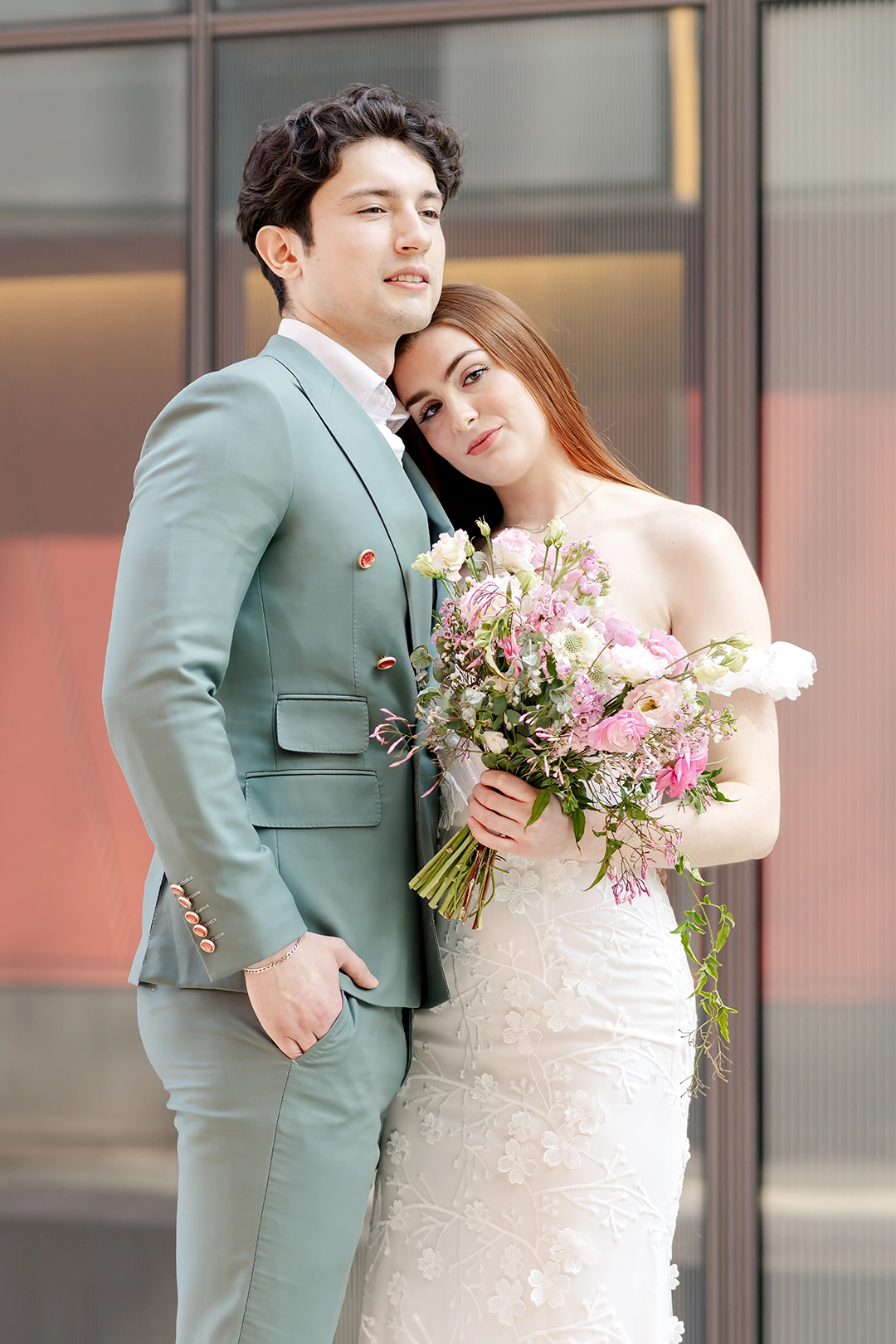 Bride and groom embracing, with the bride in a floral lace gown holding a pastel spring bouquet. The groom wears a tailored sage green suit. Captured by wedding photographer Adina Stiles, this modern city elopement highlights intentional styling and timeless romance. Perfect inspiration for elegant elopements and intimate urban weddings.