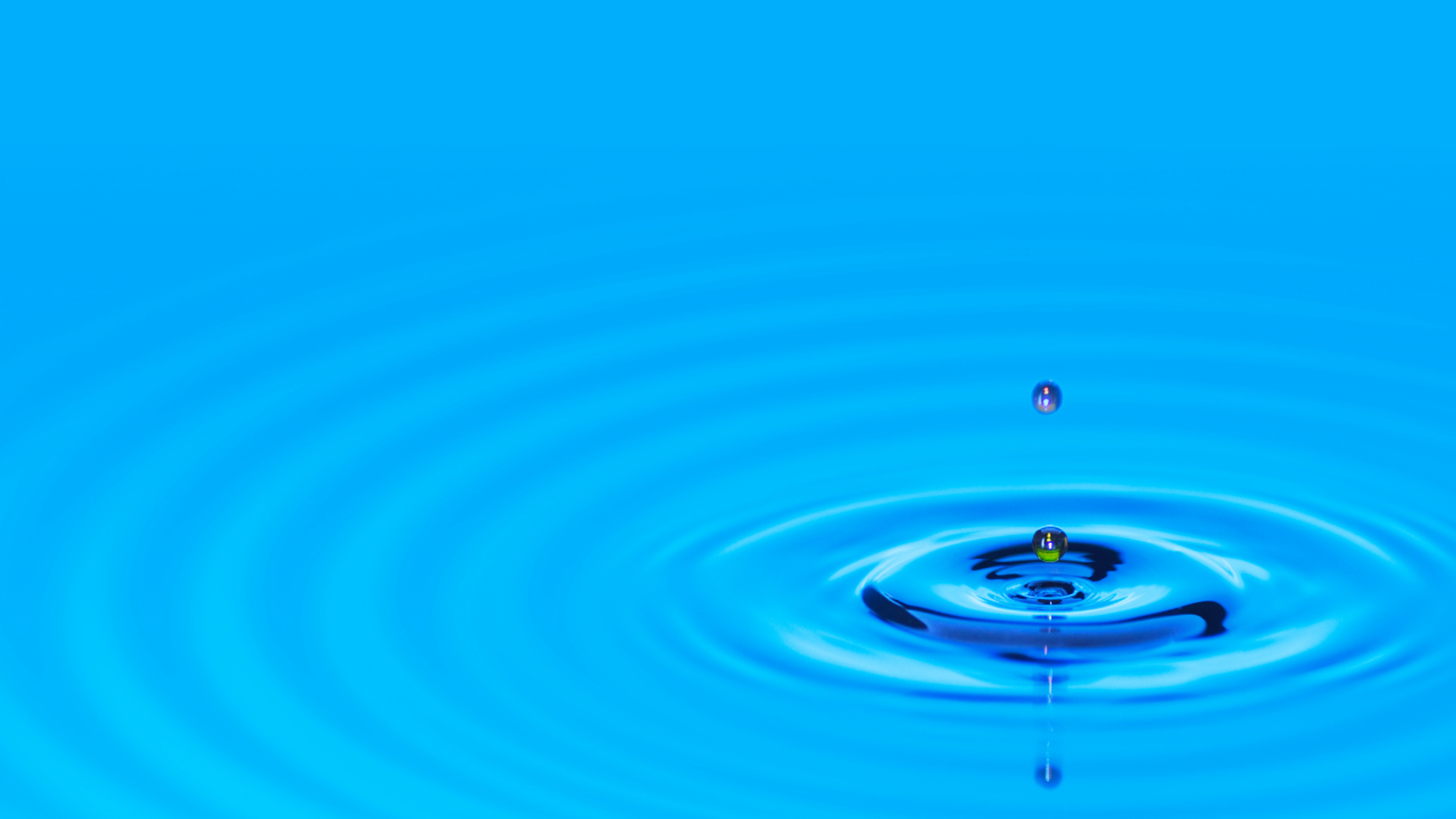 Drip into calm blue water causing circles