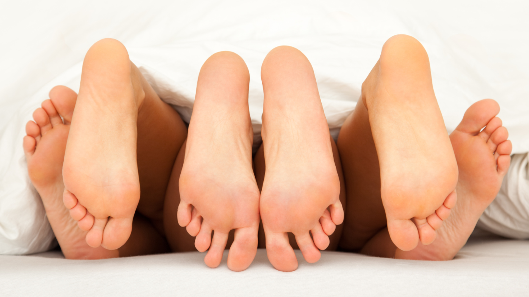 three pairs of caucasian feet poking out from a white duvet