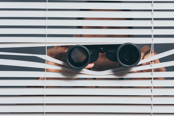 Man looking through window blinds with binoculars, symbolizing Hypervigilance in Autistic people. Man looking through window blinds with binoculars, symbolizing Hypervigilance in Autistic people.