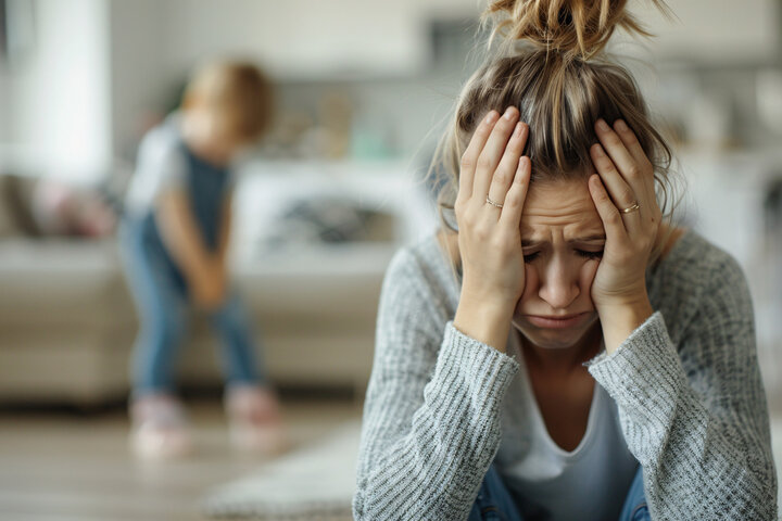 Stressed mother with head in hands and blurred child in background, representing emotional pain, parental overwhelm, and the hidden root causes behind severe autism. Stressed mother with head in hands and blurred child in background, representing emotional pain, parental overwhelm, and the hidden root causes behind severe autism.