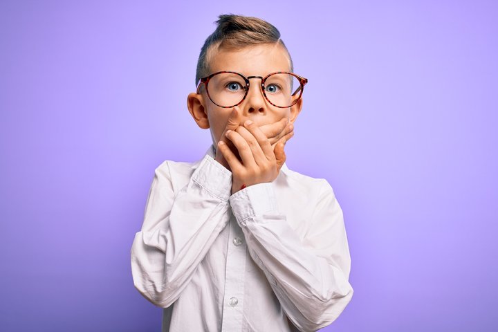 Young boy with glasses covering his mouth in surprise or silence, representing non-verbal expression in severe autism and the effects of the creative mind state on communication. Young boy with glasses covering his mouth in surprise or silence, representing non-verbal expression in severe autism and the effects of the creative mind state on communication.