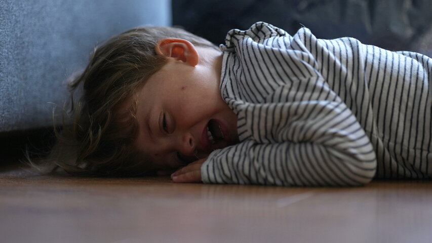 Young child lying on the floor crying during a meltdown, illustrating how severe autism behaviors are expressions of emotional overload, not intentional defiance or disorder. Young child lying on the floor crying during a meltdown, illustrating how severe autism behaviors are expressions of emotional overload, not intentional defiance or disorder.