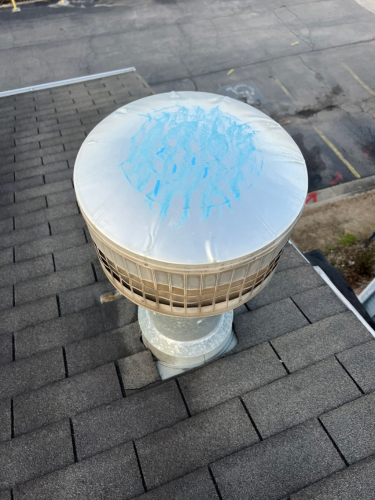 A rooftop vent with a white cap showing signs of hail damage highlighted with blue chalk. The chalk outlines numerous dents and impact marks, clearly indicating the extent of the hail damage. The vent is situated on a grey shingled roof, with the surrounding area visible in the background. A rooftop vent with a white cap showing signs of hail damage highlighted with blue chalk. The chalk outlines numerous dents and impact marks, clearly indicating the extent of the hail damage. The vent is situated on a grey shingled roof, with the surrounding area visible in the background.
