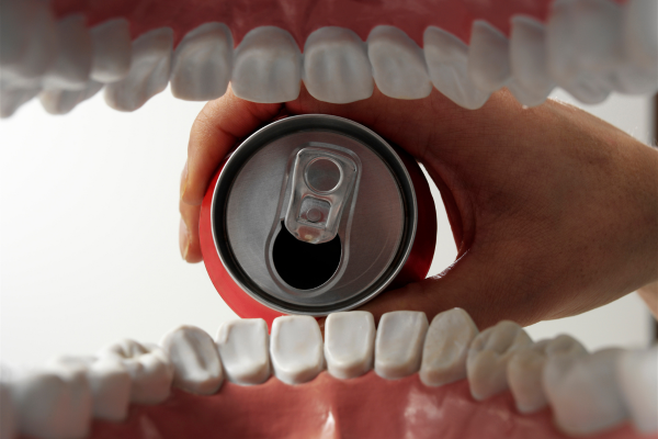 Energy drinks and soda cans next to an illustration of teeth with enamel erosion Energy drinks and soda cans next to an illustration of teeth with enamel erosion