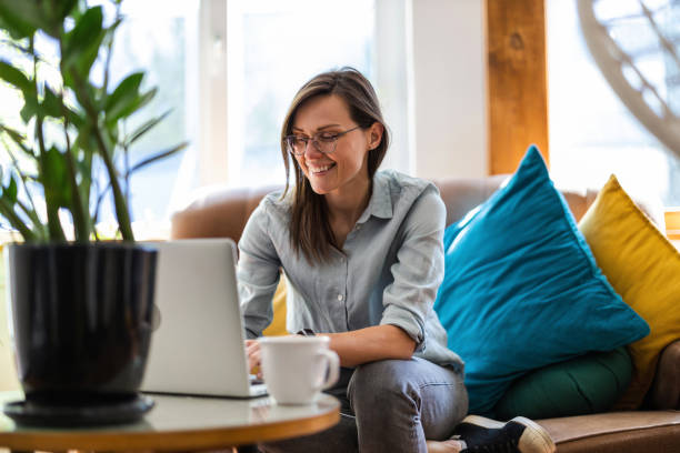 A woman works from her home office while smiling and using a laptop.