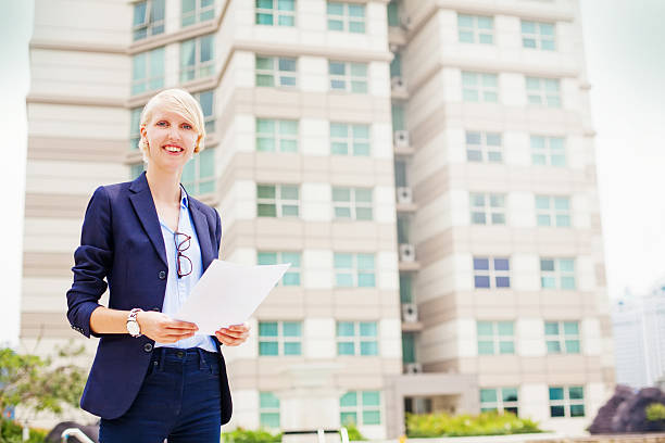 A professional insurance agent in a suit, standing in front of a modern office building with a friendly and confident smile.