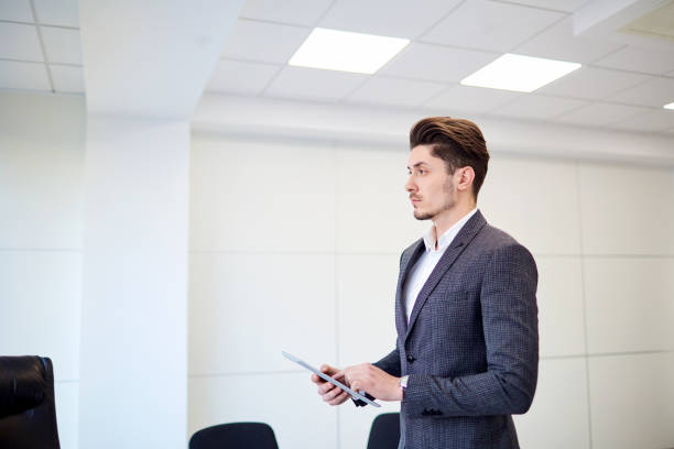 Aspiring insurance agent formally dressed man sits upright at a small corner office table confidently waiting - representing a job seeker in the insurance industry