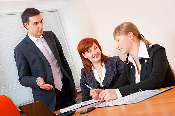 A confident insurance agent presenting to attentive clients in a modern office setting.