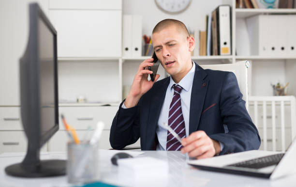A professional insurance broker in an office, engaged in client communication and work on a computer.