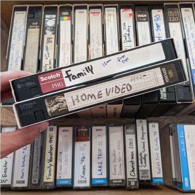 Two labeled VHS tapes, “Family” and “Home Video,” held in front of a collection of old home movies and family recordings. Two labeled VHS tapes, “Family” and “Home Video,” held in front of a collection of old home movies and family recordings.