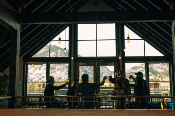 crowd enjoying beers with each other looking out a window at a mountain