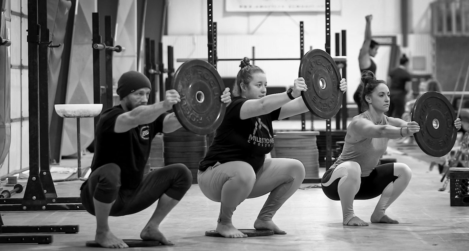 Three lifters performing mobility exercises with weight plates in a gym, demonstrating the importance of flexibility and balance in strength training. Focus on deep squats for enhanced performance and injury prevention in lifting. Three lifters performing mobility exercises with weight plates in a gym, demonstrating the importance of flexibility and balance in strength training. Focus on deep squats for enhanced performance and injury prevention in lifting.